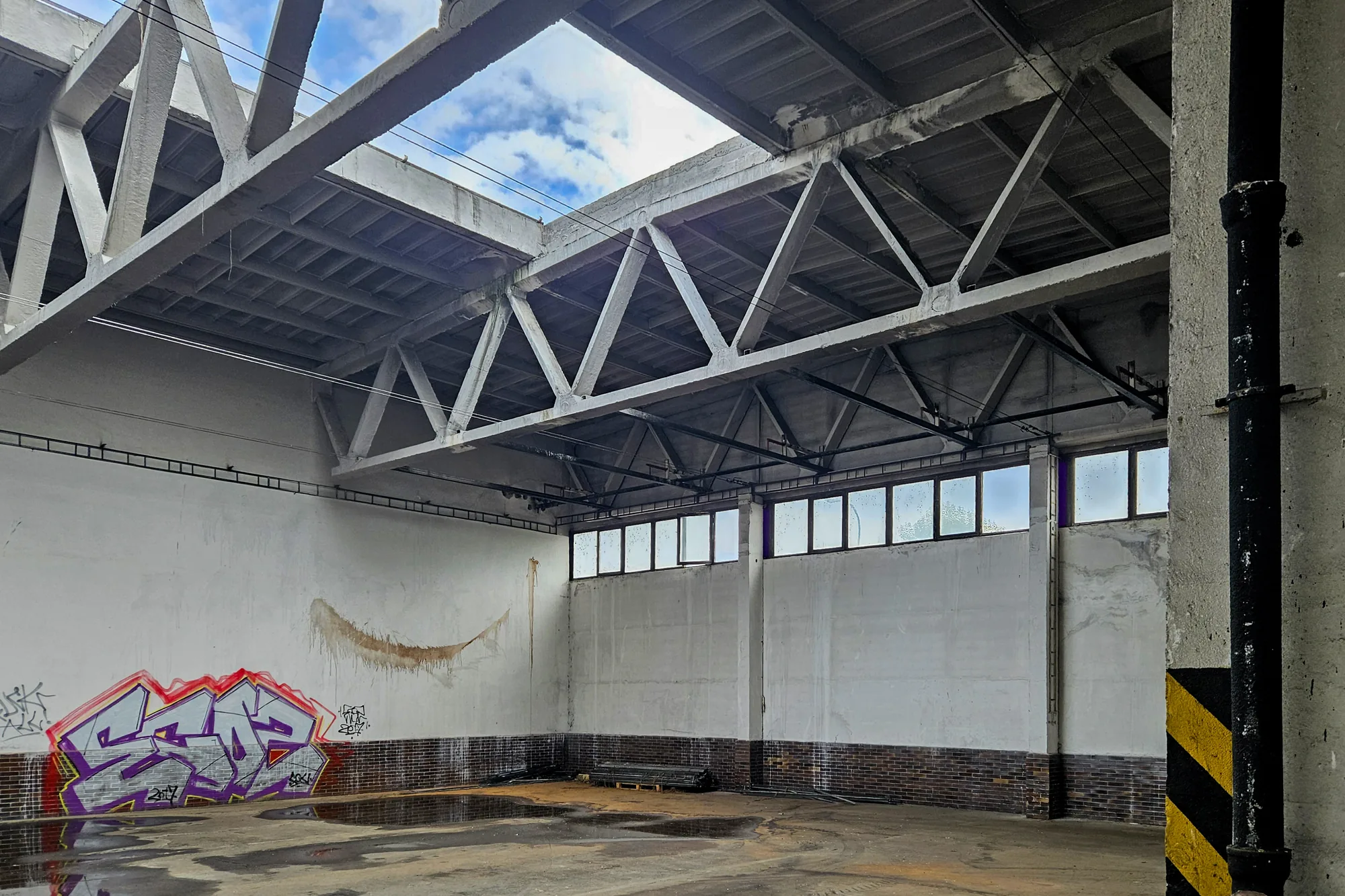 Close view of two IDA roof trusses against the sky: parallel concrete chords joined by a triangular pattern of diagonals only, with no vertical members, no joints along the chords and plain concrete at the ends