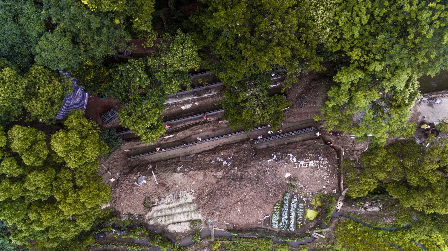 Aerial view of the sloped site with terraced retaining walls under construction