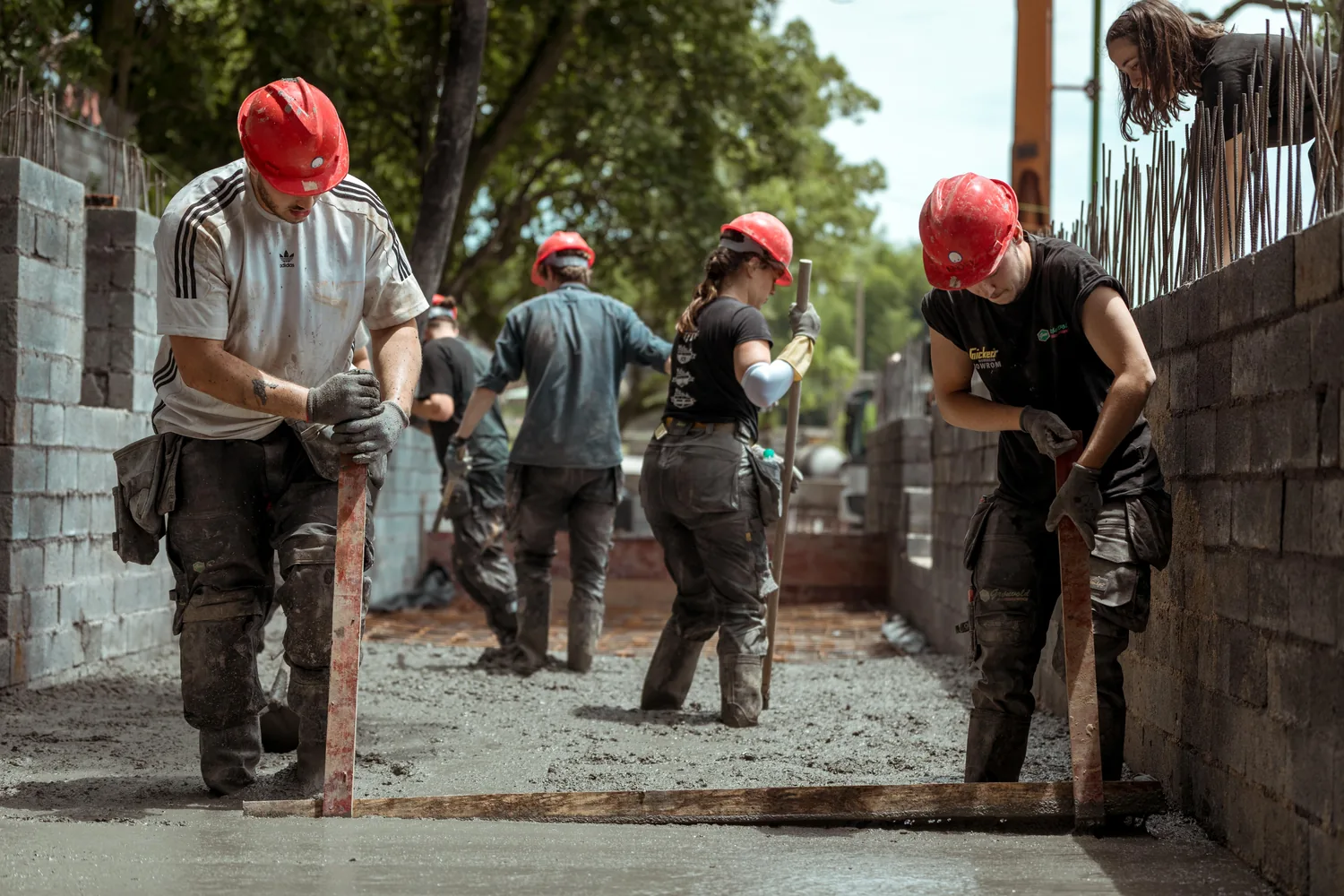Students screeding a wet concrete floor slab between block walls