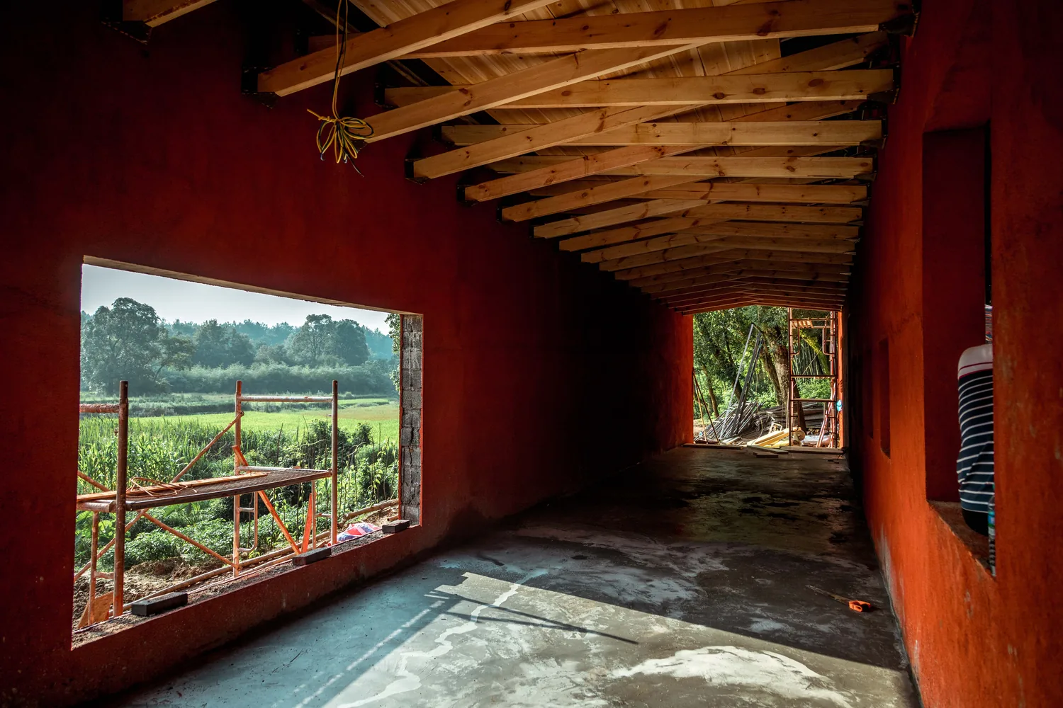 Red-walled interior with timber roof beams and a window onto fields